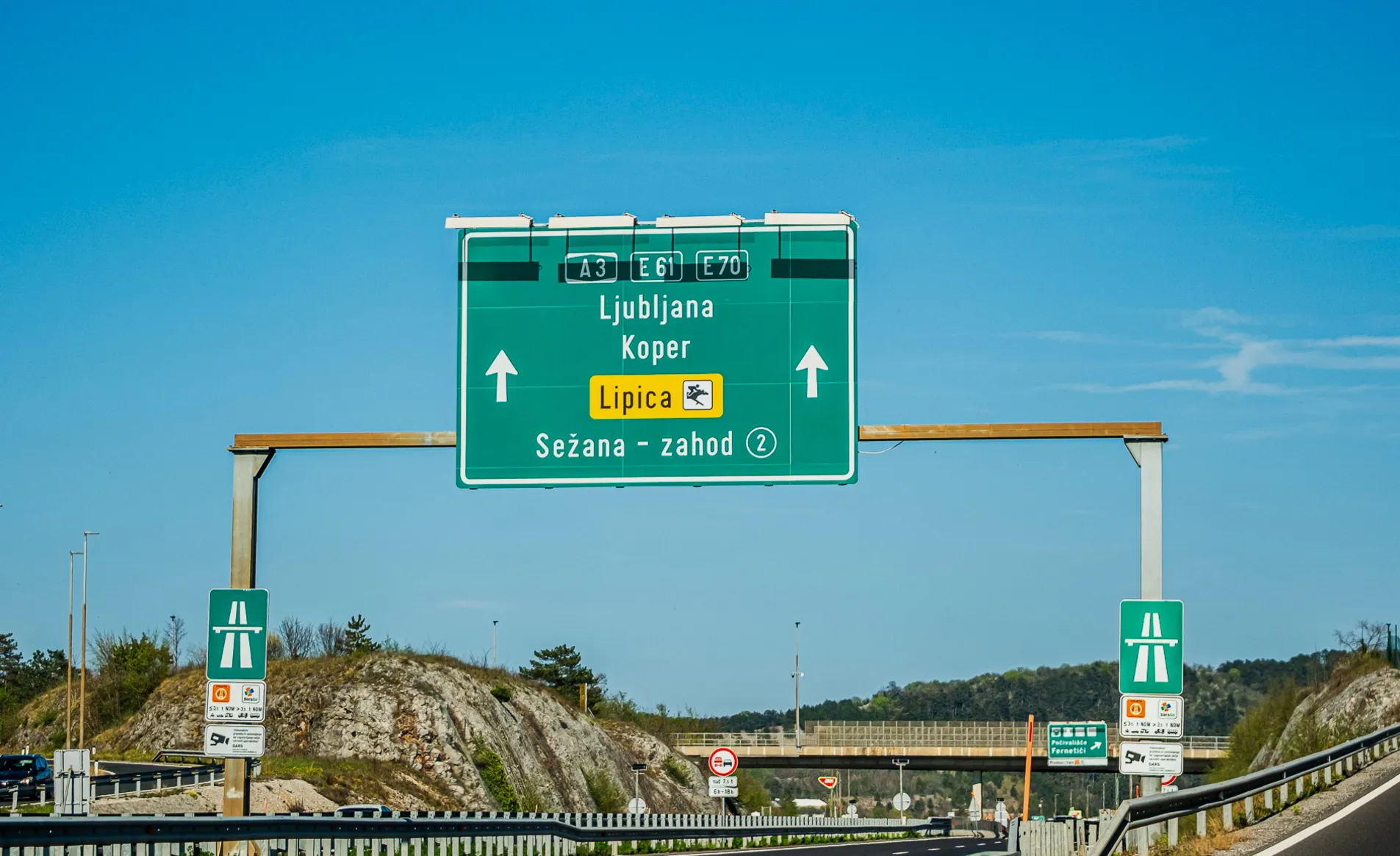 Slovenia A3 E61 E70 motorway overhead signs directing to Ljubljana, Koper and Lipica with Sežana-zahod exit 2, e-vinjeta and DarsGo payment signs visible on gantry posts, April 2026